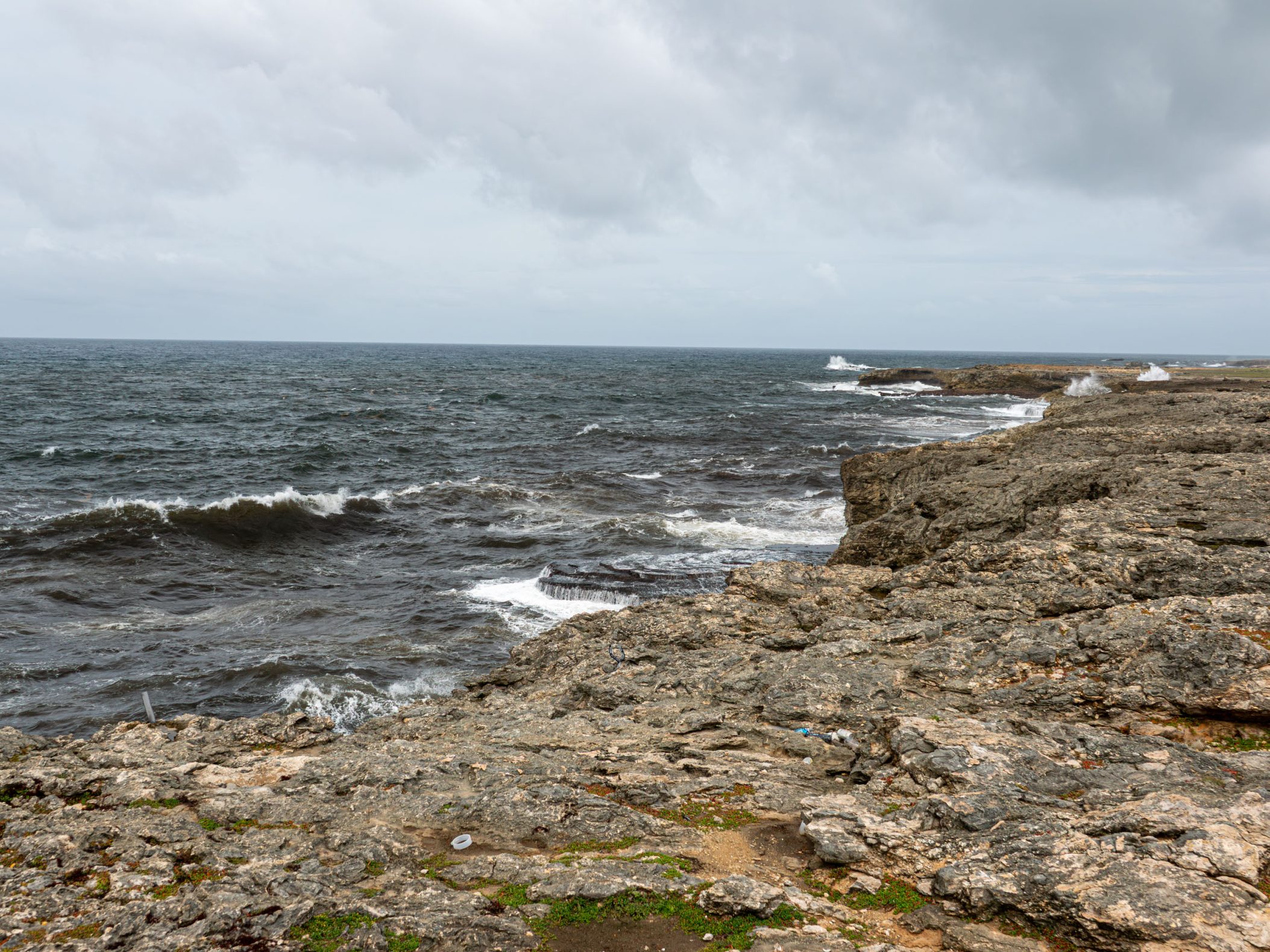 Wide view of brown cliffs with choppy ocean crashing in to it