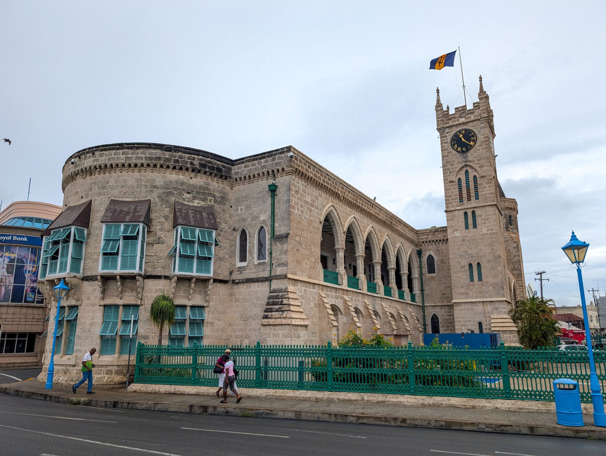 Large brick building with windows and a clock tower with Barbados flag