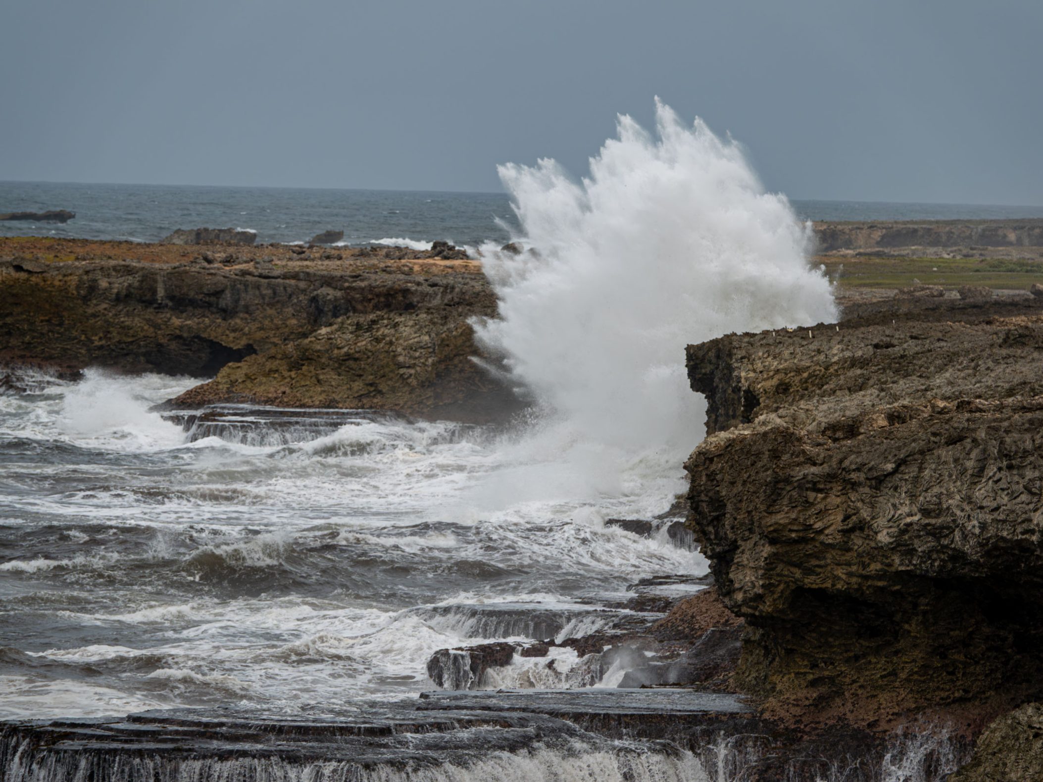A large wave crashing in to brown cliffs